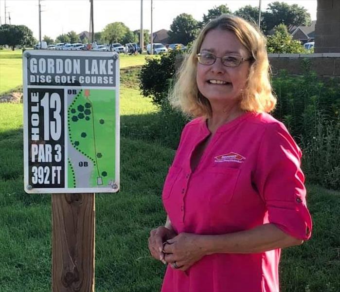 female in pink shirt standing on golf course by hole 13 sign