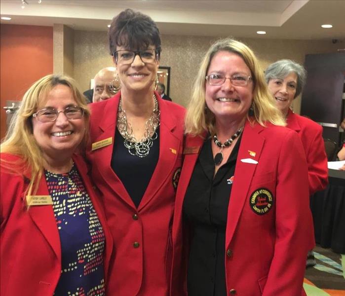 Three ladies in red coats welcome meeting attendees